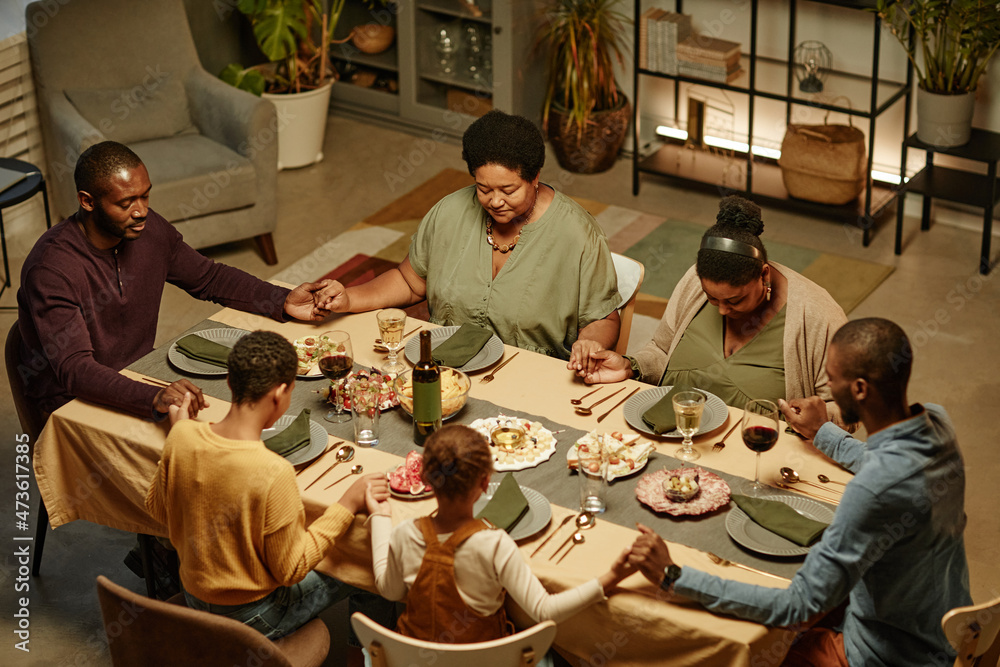 High angle view at big African-American family holding hands while saying grace during dinner party at home