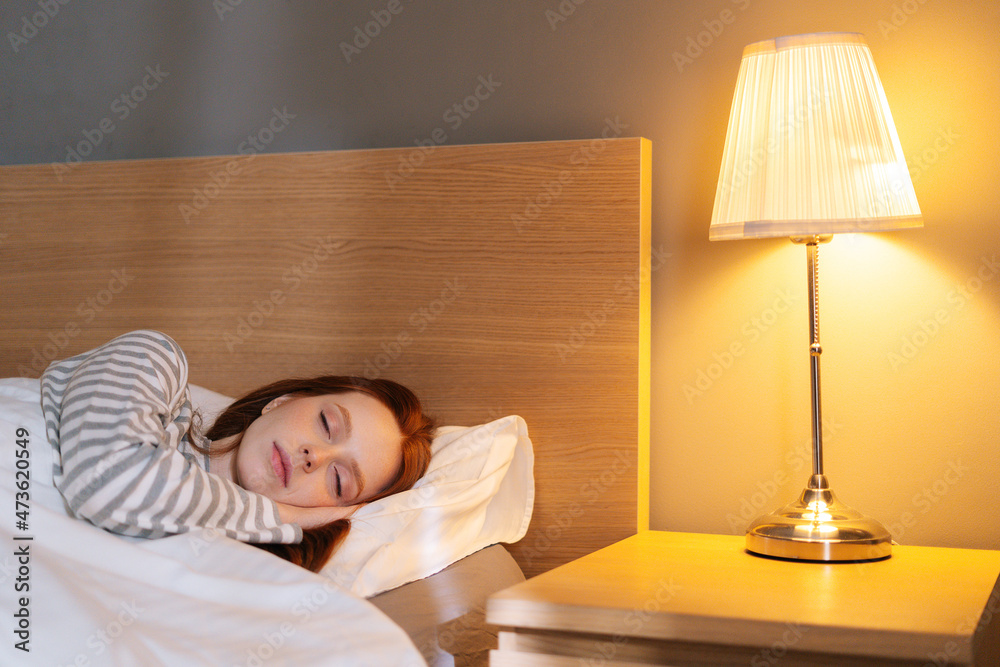 Close-up face of tired young woman sleeping well in bed hugging soft white  pillow at