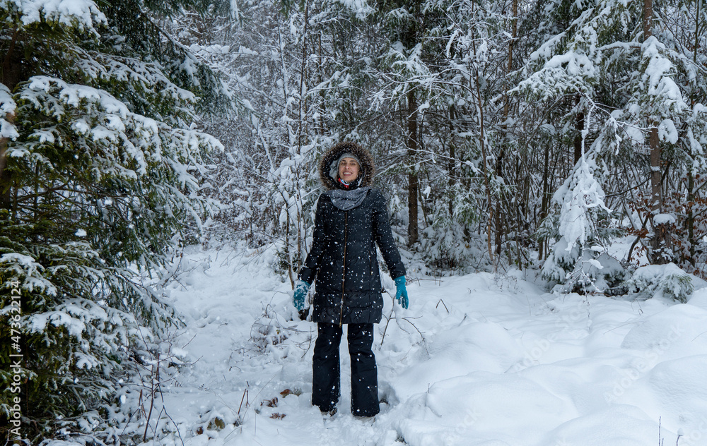 Naklejka premium Caucasian woman in winter forest. Girl enjoys the snow falls. Have a good time outdoor in a snowy forest. Attractive young woman in wintertime outdoor.