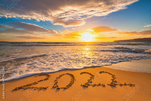 Fototapeta Naklejka Na Ścianę i Meble -  Happy New Year 2022 concept, lettering on the beach. Written text on the sea beach at sunrise.