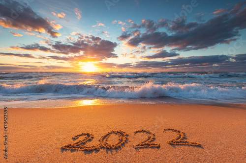 Happy New Year 2022 text, lettering on the beach sand at sunrise.