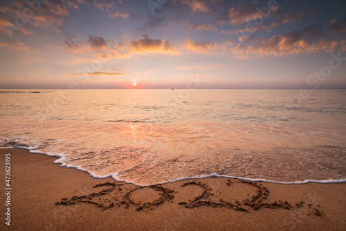 Fototapeta Naklejka Na Ścianę i Meble -  Sea sunrise over the beach. New year 2022 text on the sand.