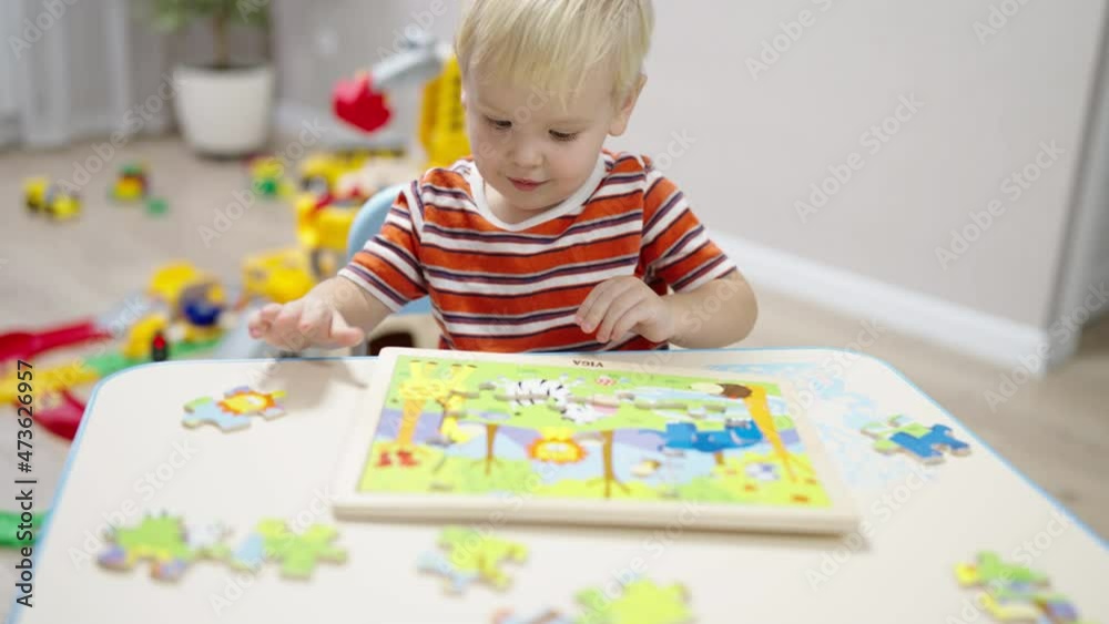 little boy with blond hair sits at the table and collects wooden puzzles little boy with blond hair sits at the table and collects wooden puzzles