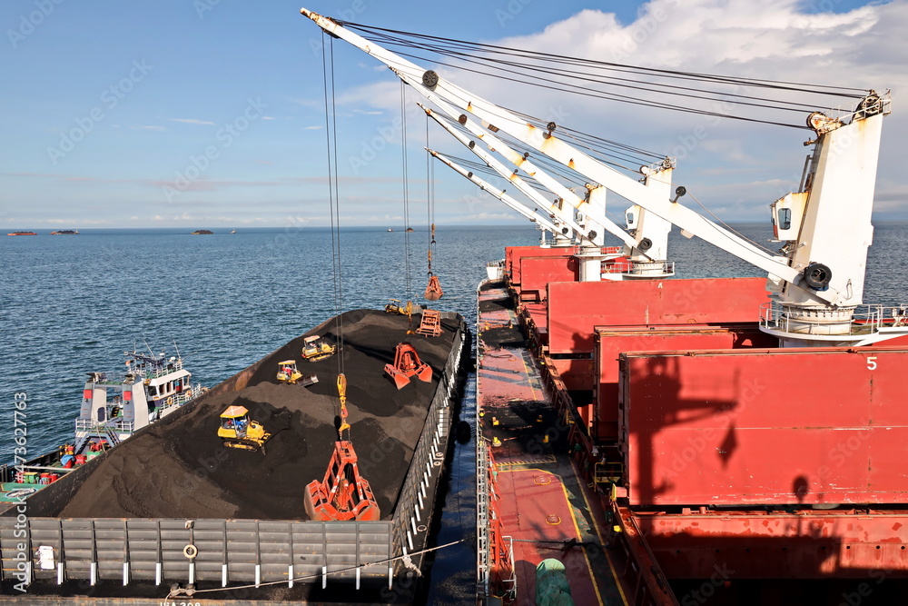 Loading coal from cargo barges onto a bulk carrier using ship cranes