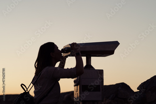 Young woman looking through a coin operated binoculars in the dark