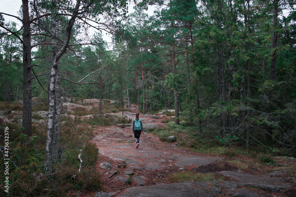 Woman hiking through green forest in Tyresta National Park in Sweden.
