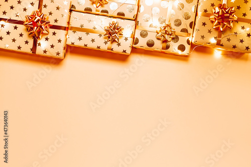 Gift boxes with golden bows and lights on peach background. Copy space for your text. Top view. photo