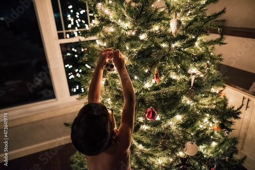 Back of child hanging ornament on tree. 