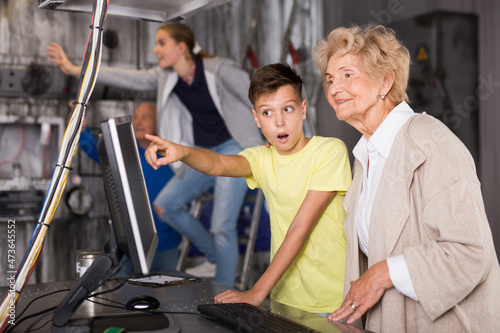 Young boy and his grandmother using computer to solve conundrum in escape room. Teenager girl standing on stepladder and reaching hand in background.