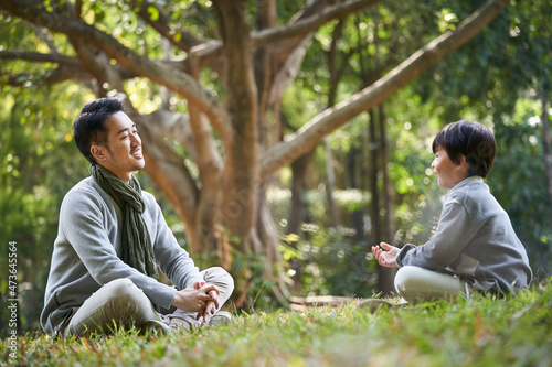 asian father and son having a conversation outdoors in park