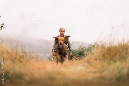 Mature hunting man and his dog chasing a prey across the field.