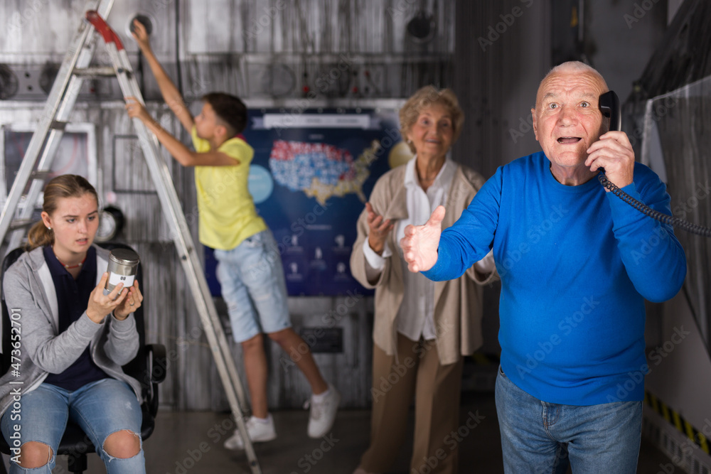 Obraz premium Grandparents and grandchildren failed at escape room. Old man talking on phone with administrator of about letting them out.