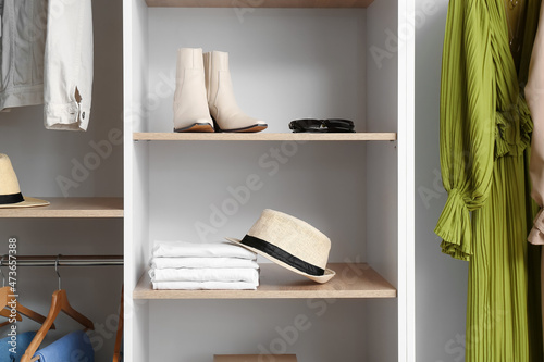 Stylish hat, clothes and shoes on shelves in wardrobe