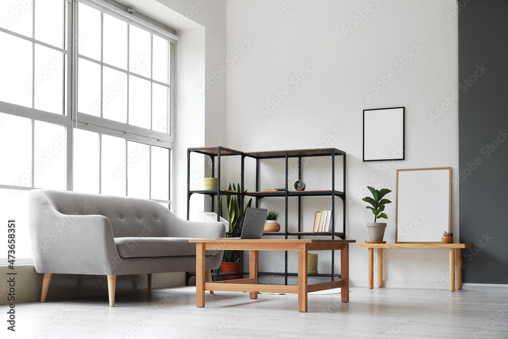 Fototapeta premium Modern living room interior with gray sofa, wooden coffee table, metal shelving unit, and blank picture frames