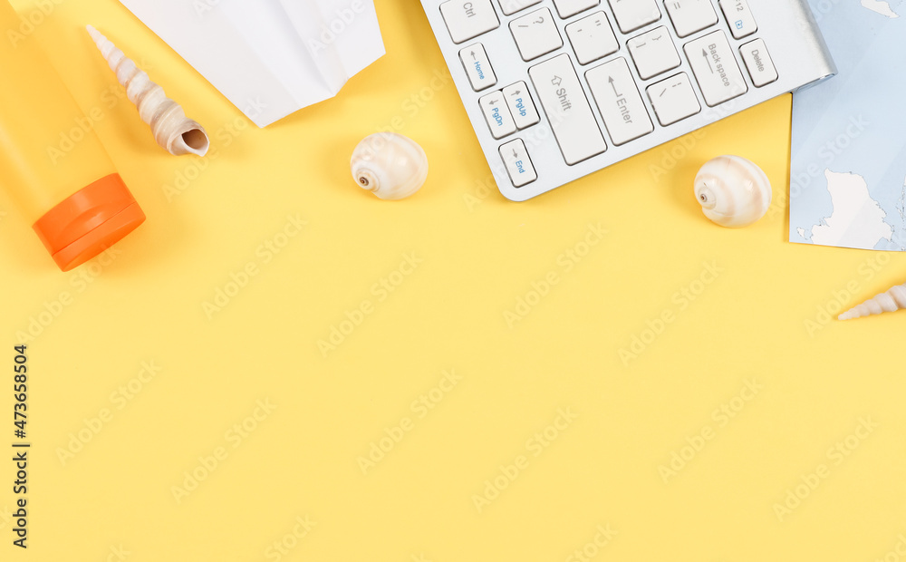 Keyboard, world map, seashells, paper plane and sun cream on light yellow Keyboard, world map, seashells, paper plane and sun cream on light yellow