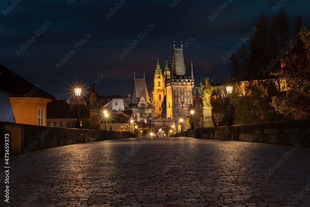 Naklejka premium .old cobbled sidewalk with paving Charles Bridge in the center of Prague and in the background the old bridge tower at night in the Czech Republic and the light from street lighting