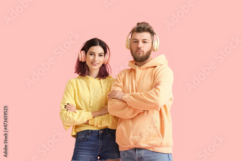 Cool young couple in hoodies listening to music on color background