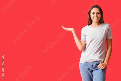 Young woman in blank t-shirt showing something on color background