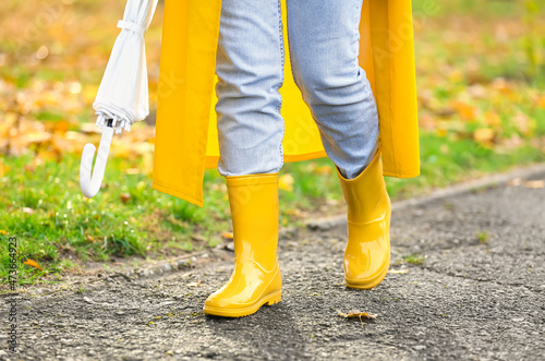 Woman with umbrella wearing yellow raincoat and gumboots walking in autumn park