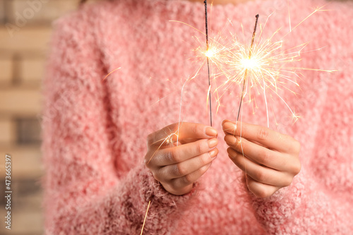 Woman in pink sweater holding Christmas sparklers on brick background, closeup