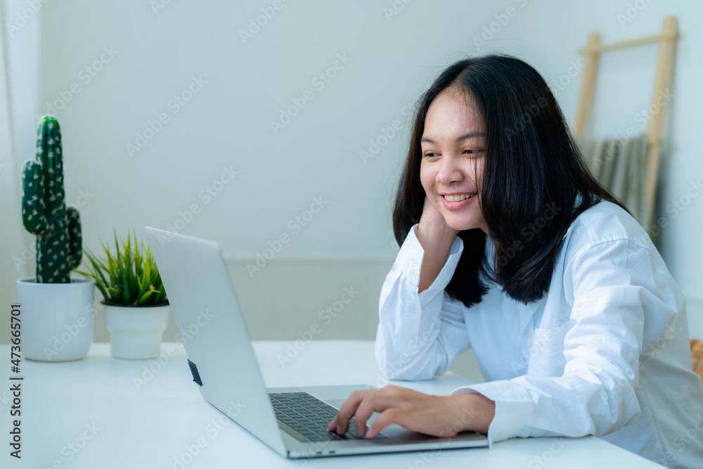 Portrait Cute Asian teen with long hair Wearing a white shirt, sitting happily studying online with a laptop on the bedroom desk. Portrait Cute Asian teen with long hair Wearing a white shirt, sitting happily studying online with a laptop on the bedroom desk.