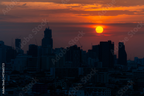 The sun was setting in the evening, a golden orange light shone all around. with a backdrop of tall buildings in a large city in the shadows © Ekkasit A Siam