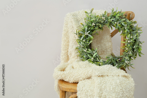 Wooden chair with plaid and Christmas wreath with mistletoe near light wall