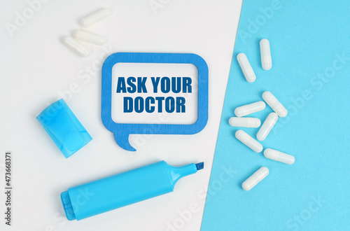 On a white and blue table are pills, a marker and a blue plaque with the inscription - ASK YOUR DOCTOR