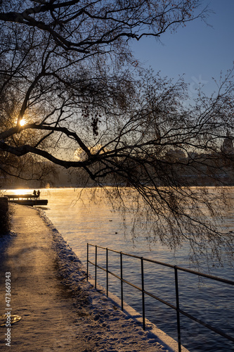 People walking on a walking path at Stockholm bay on freezing winter day with steaming water, birch tree in front and cozy sun light. Winter time in capital of Sweden   © boumenjapet
