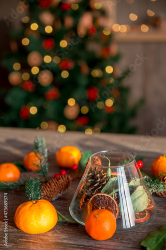 New Year's composition of tangerines, cones and Christmas tree branches on a wooden table. Against the background of a sparkling Christmas tree. Preparing for the holiday