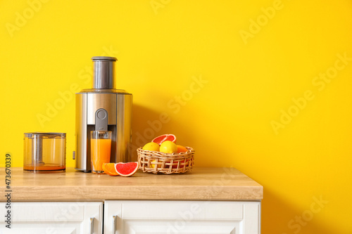 Modern juicer with fresh citrus fruits and glass of juice on table in kitchen
