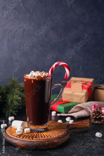 Glass cup of tasty hot chocolate with marshmallows and candy cane on black background