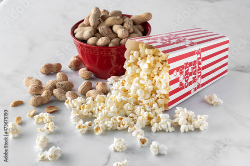 Photography Close up of a container of popcorn tipped over with a bowl of peanuts in behind