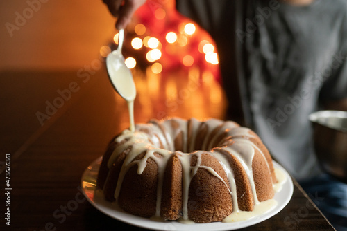 Person decorates bundt cake with drizzled glaze
 photo