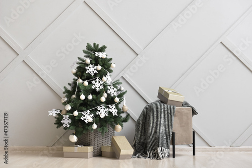 Beautiful Christmas tree in basket decorated with snowflakes  balls  pouf and gift boxes near light wall
