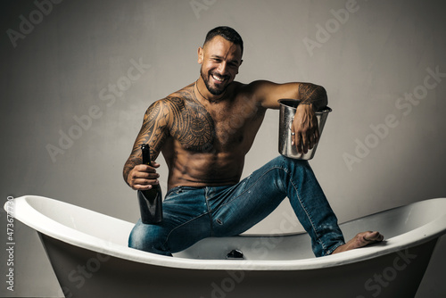 Sexy smiling man sit on bathtub in bathroom, men holiday with champagne. Celebrating christmas or birthday. Private sex party.