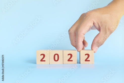 Year 2022 conclusion, review, summary and finishing annual report concept. Hand finishing building blocks with 2022 number in blue background.