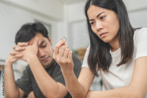 Stress, unhappy asian young couple man, woman quarrel on couch, relationship in trouble. Wife holding wedding ring in disappointment and upset her husband, which may lead to divorce. Problem of family