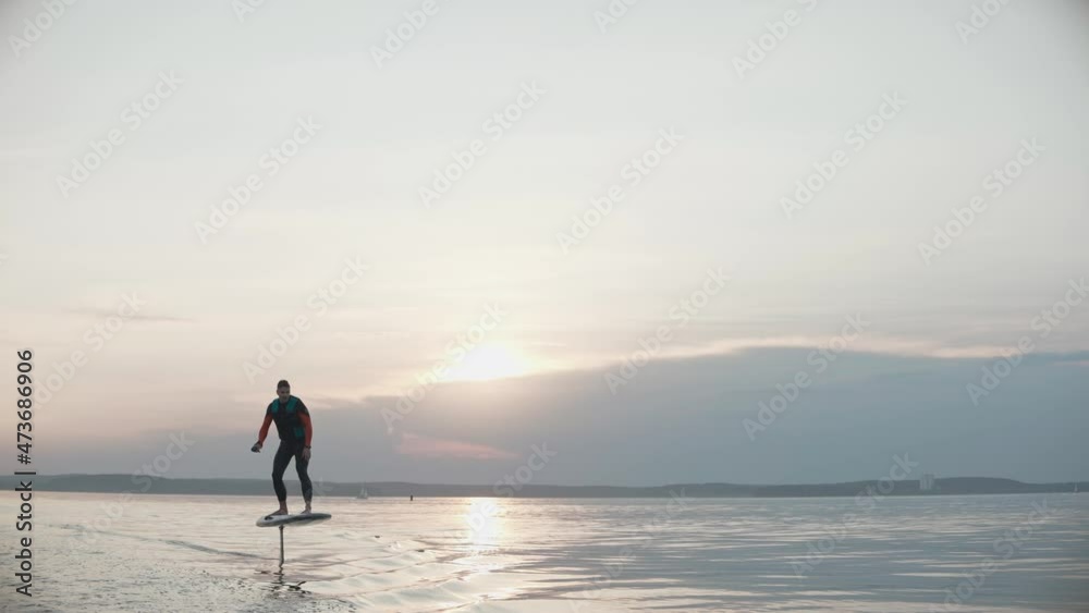 Man riding on a hydrofoil surfboard on large lake at golden sunset. Shot of man riding a hydrofoil surfboard in the middle of the lake. High quality 4k footage Man riding on a hydrofoil surfboard on large lake at golden sunset. Shot of man riding a hydrofoil surfboard in the middle of the lake. High quality 4k footage
