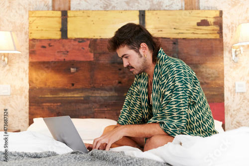 Young gay man using a laptop on his bed photo