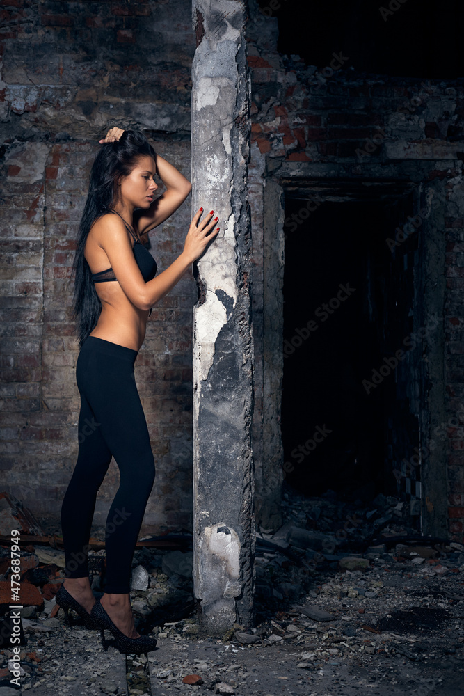 Young beautiful woman posing in ruins after fire. Full-length view of brick wall and concrete pillar. Сopy space
