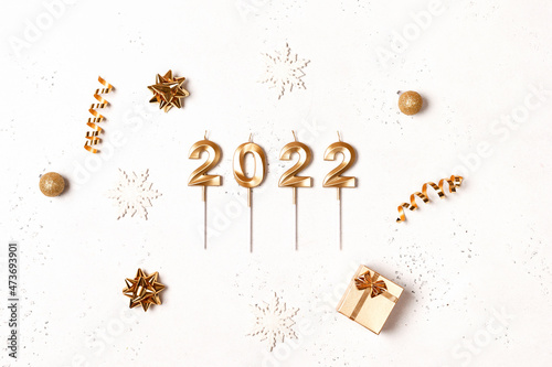 Christmas frame with golden decorations on white background with festive golden numbers 2022 made of candles in the center. New year concept. Flat lay, top view, copy space