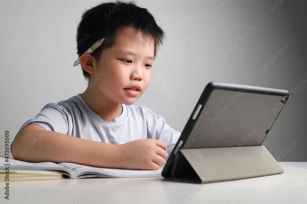 Portrait of a little Asian boy using tablet computer during pandemic lockdown, homeschooling, social distance, stay at home, online education concept. Portrait of a little Asian boy using tablet computer during pandemic lockdown, homeschooling, social distance, stay at home, online education concept.