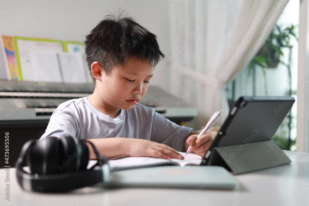 Portrait of a little Asian boy using tablet computer during pandemic lockdown, homeschooling, social distance, stay at home, online education concept. Portrait of a little Asian boy using tablet computer during pandemic lockdown, homeschooling, social distance, stay at home, online education concept.