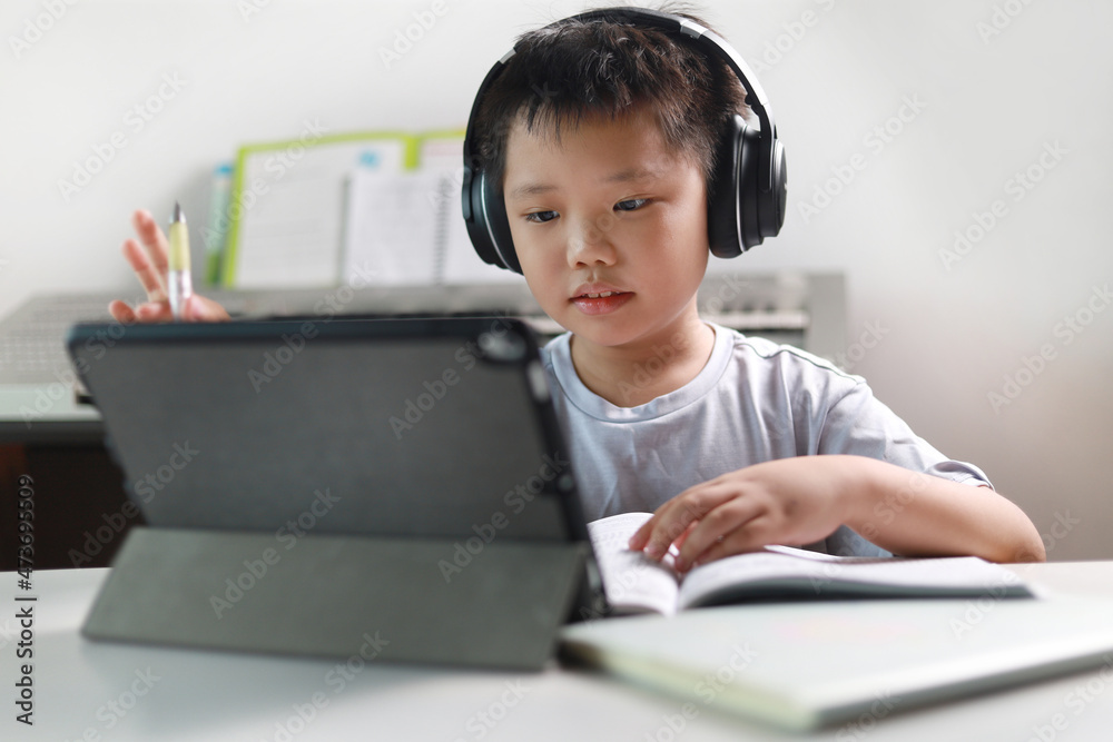 Portrait of a little Asian boy using tablet computer and headphone during pandemic lockdown, homeschooling, social distance, stay at home, online education concept. Portrait of a little Asian boy using tablet computer and headphone during pandemic lockdown, homeschooling, social distance, stay at home, online education concept.