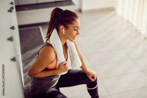 Young athletic woman listens music over wireless earphones in dressing room at gym. photo