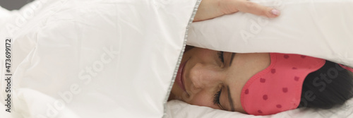 Woman lies in bed covering head with blanket closeup photo