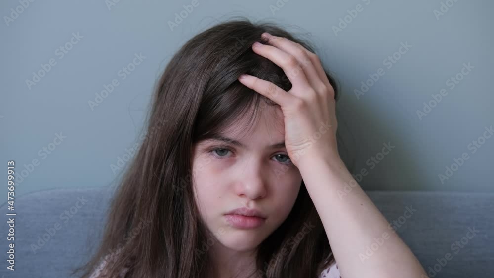 Little girl, teenager is sick, holding her head, unhappy looking at the camera Little girl, teenager is sick, holding her head, unhappy looking at the camera
