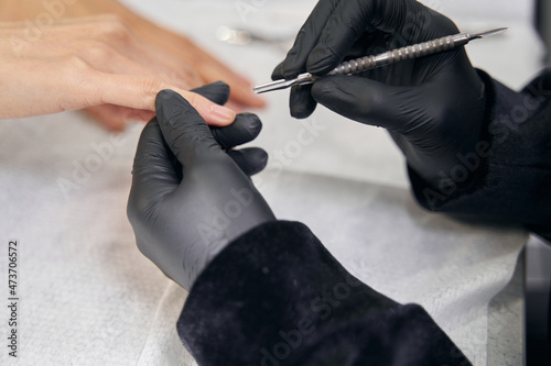 Unrecognized manicurist cleaning under the free edge of nail in beauty center
