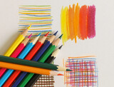 Colored pencils neatly stacked on a white sheet of paper with some drawings.